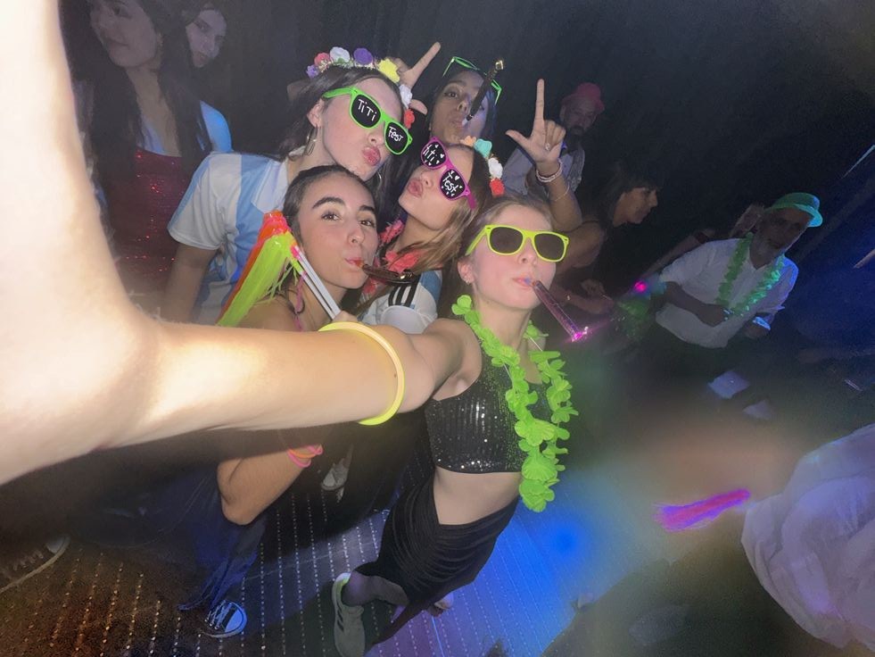 Amigas con collares verdes, lentes de colores y coronas de flores en una fiesta